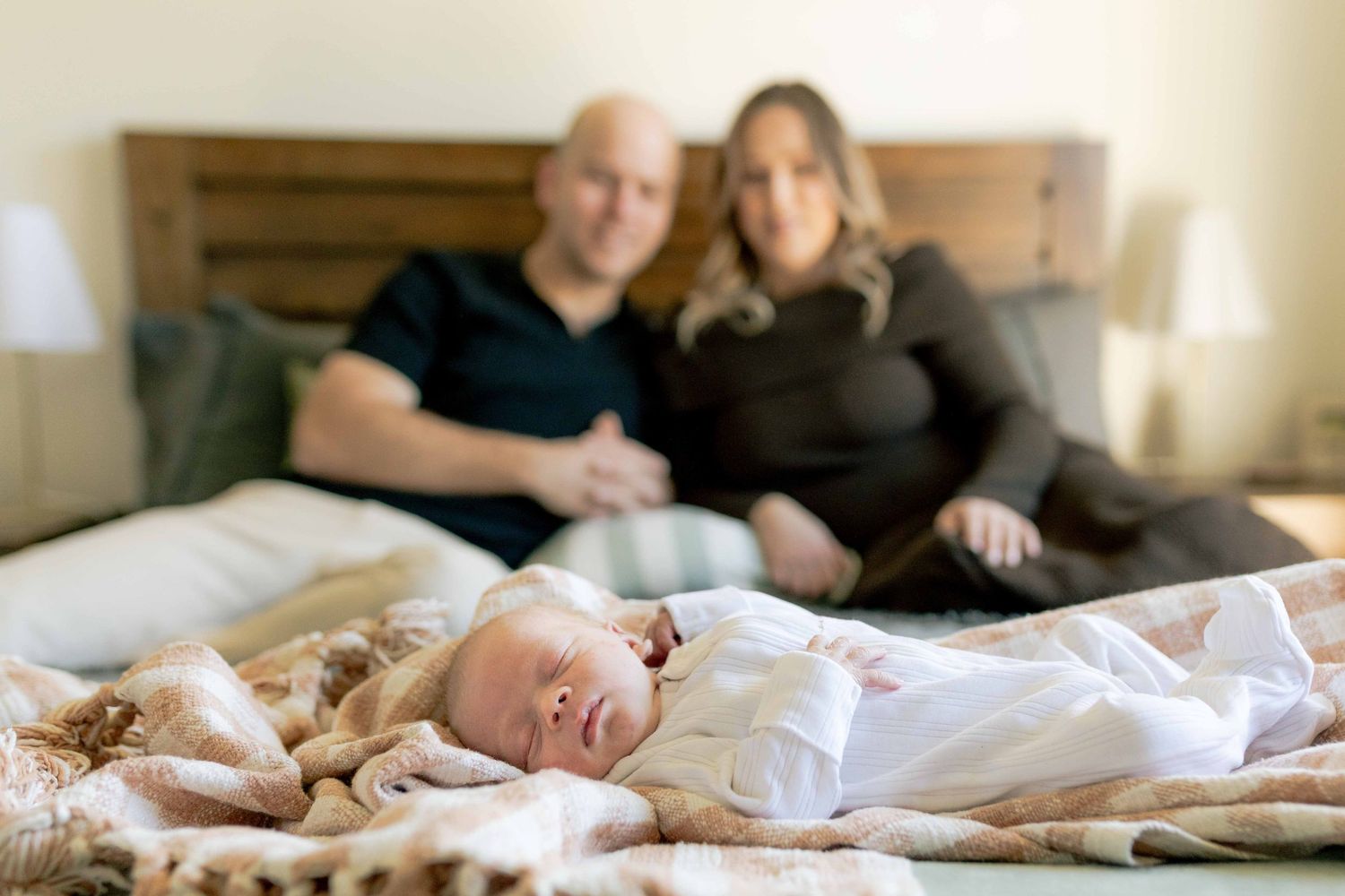 Newborn in focus parents blurred in the background sitting on the bed Melbourne's West Newborn Photography