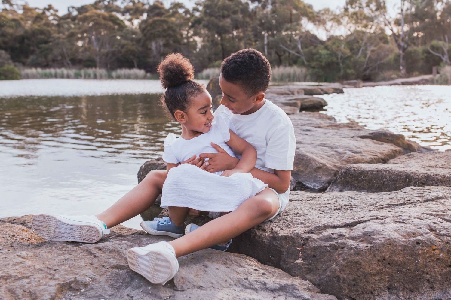Brother and sister hugging sitting on the rocks across a lake outdoor family session  Newport Lakes, Melbourne, Victoria