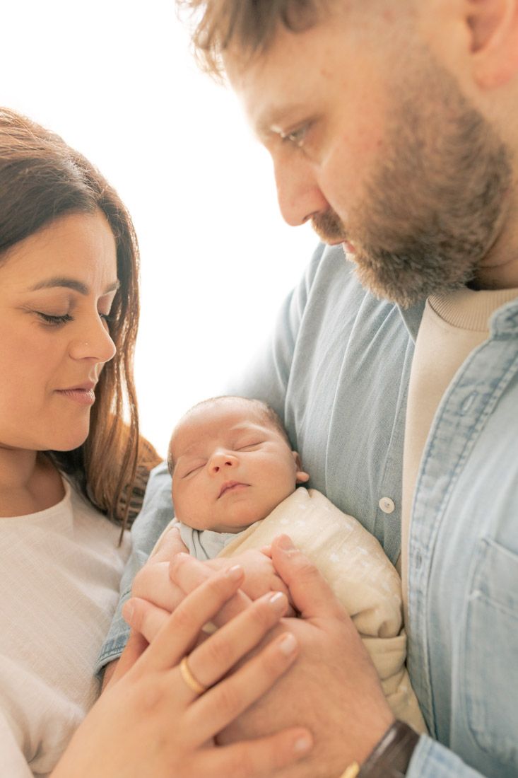parents standing close together hands on top of each other holding their newborn between them Burnside Newborn Photography