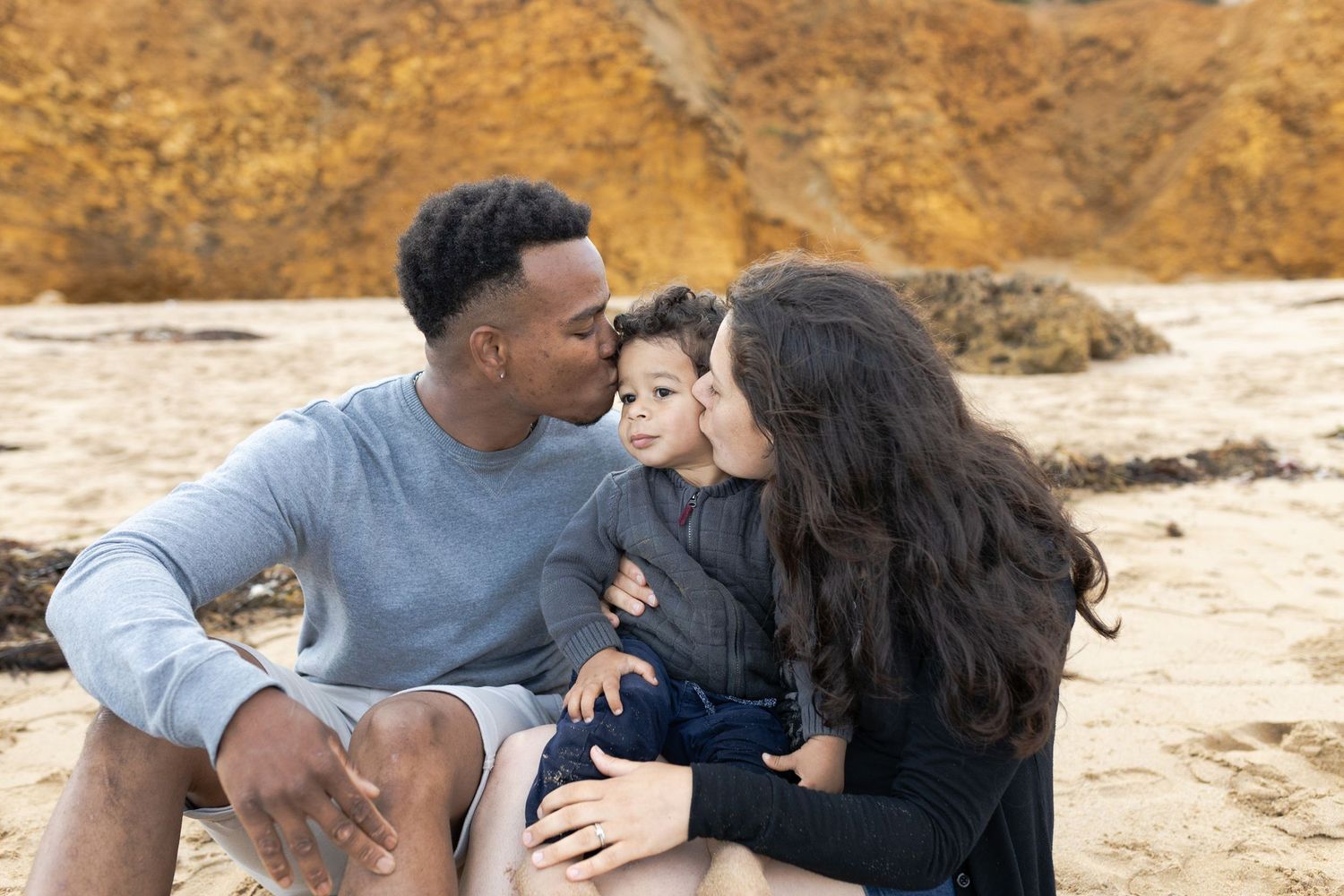 Parents kissing their son on the beach Outdoor family session Torquay