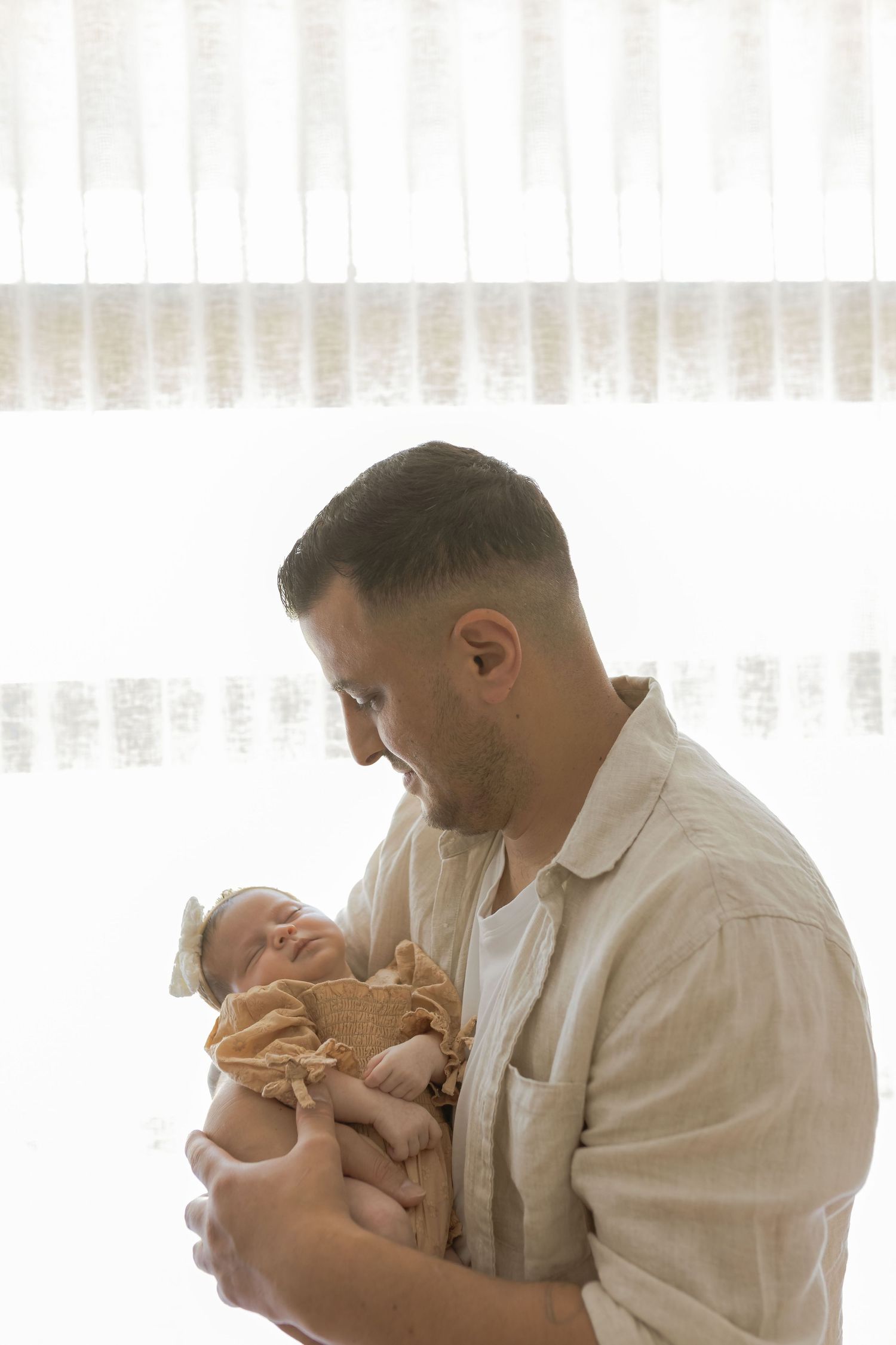 Father holding newborn daughter in front of a window at home newborn session Point Cook Melb Vic