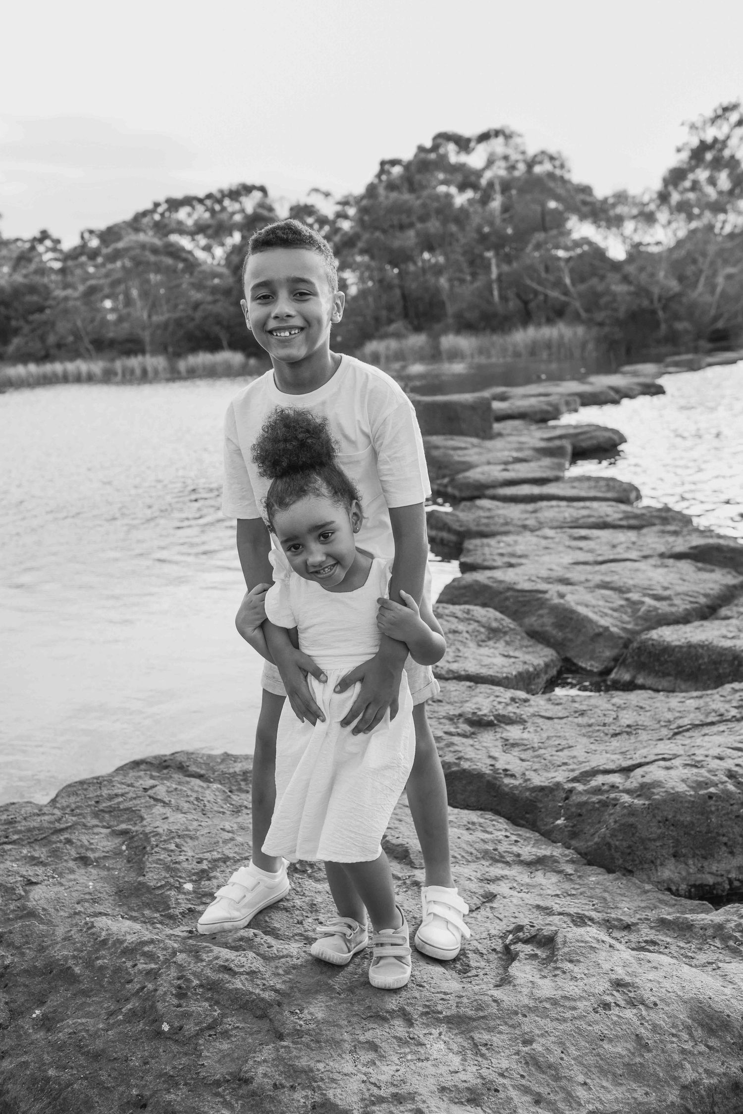 Brother and sister holding hands standing on the rocks across a lake outdoor family session Newport Lakes, Melbourne, Victoria