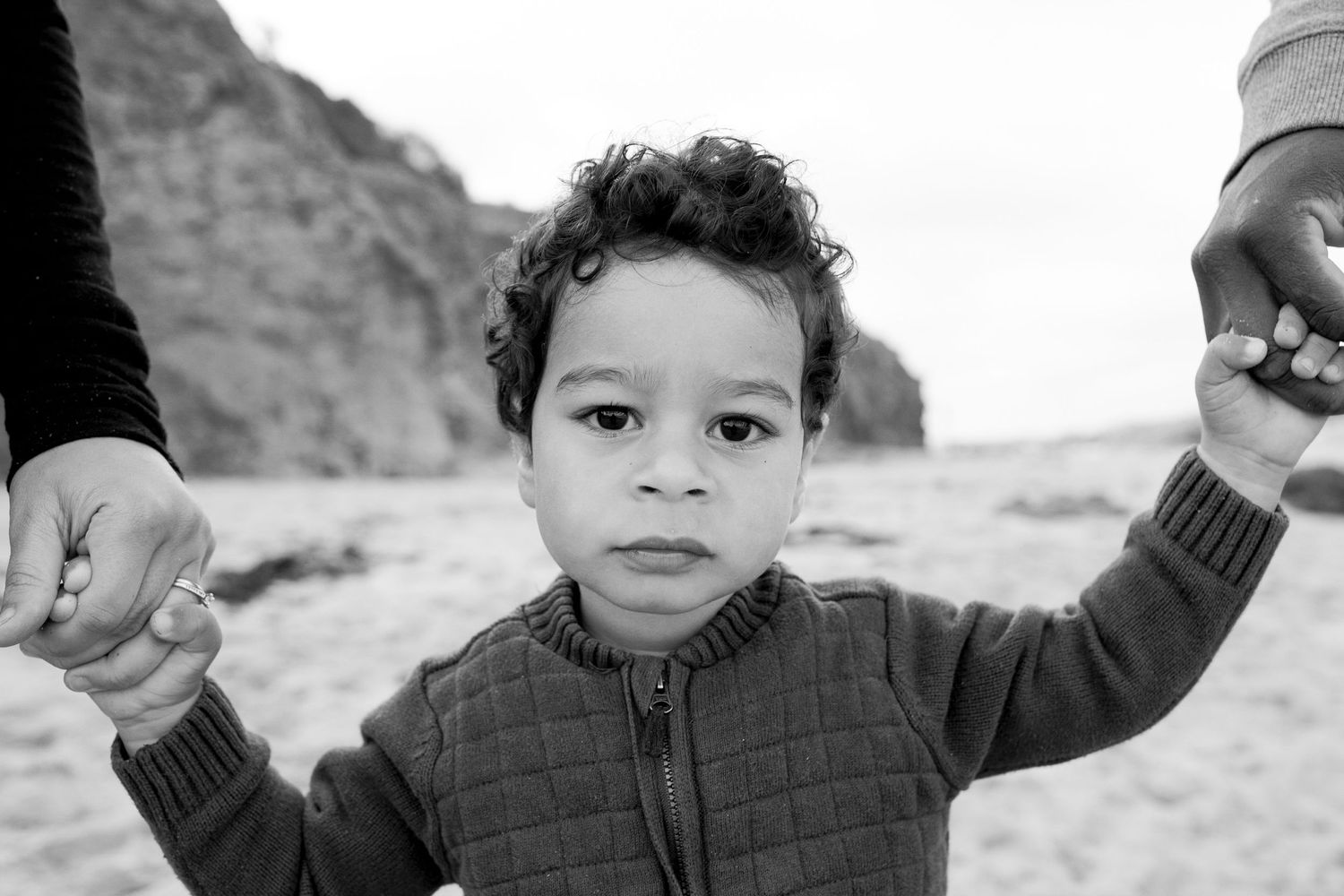 Toddler holding onto his parents hands and walking on the sand at the beach Outdoor family session Torquay