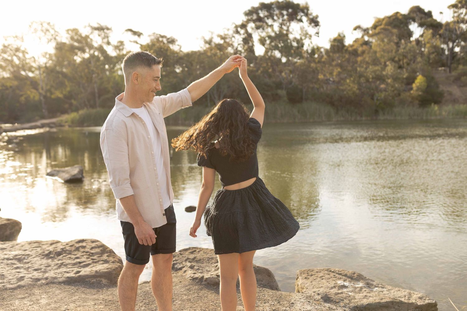 Dad twirling his daughter around on a rock wit the lake behind them, outdoor family session, Newport Lakes, Melb, Vic