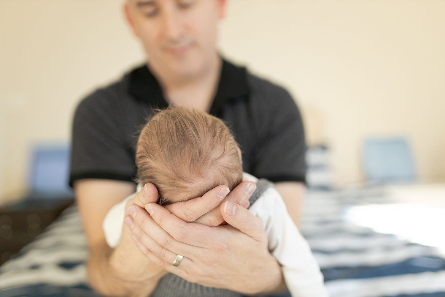 Dad holding newborn baby boy in his hands while sitting on the bed at home newborn session  Moonee Ponds Melb