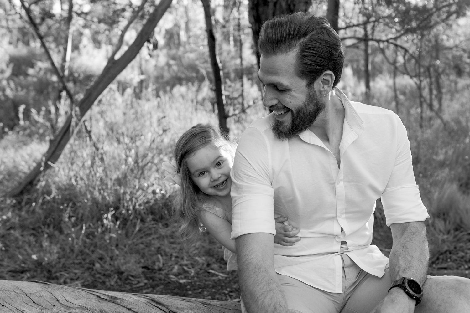Little girl playing peek a boo from behind her dad, smiling at each other outside in bushland, Sunshine North, Melb, Vic
