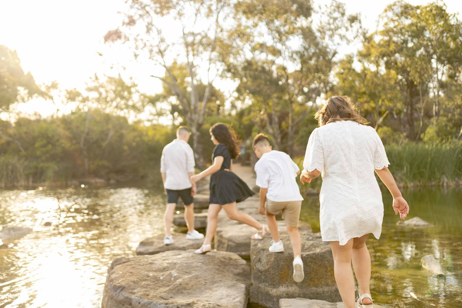 Family of four walking across the rocks on a lake following each other warm sunlight, Newport Lakes, Melb, Vic