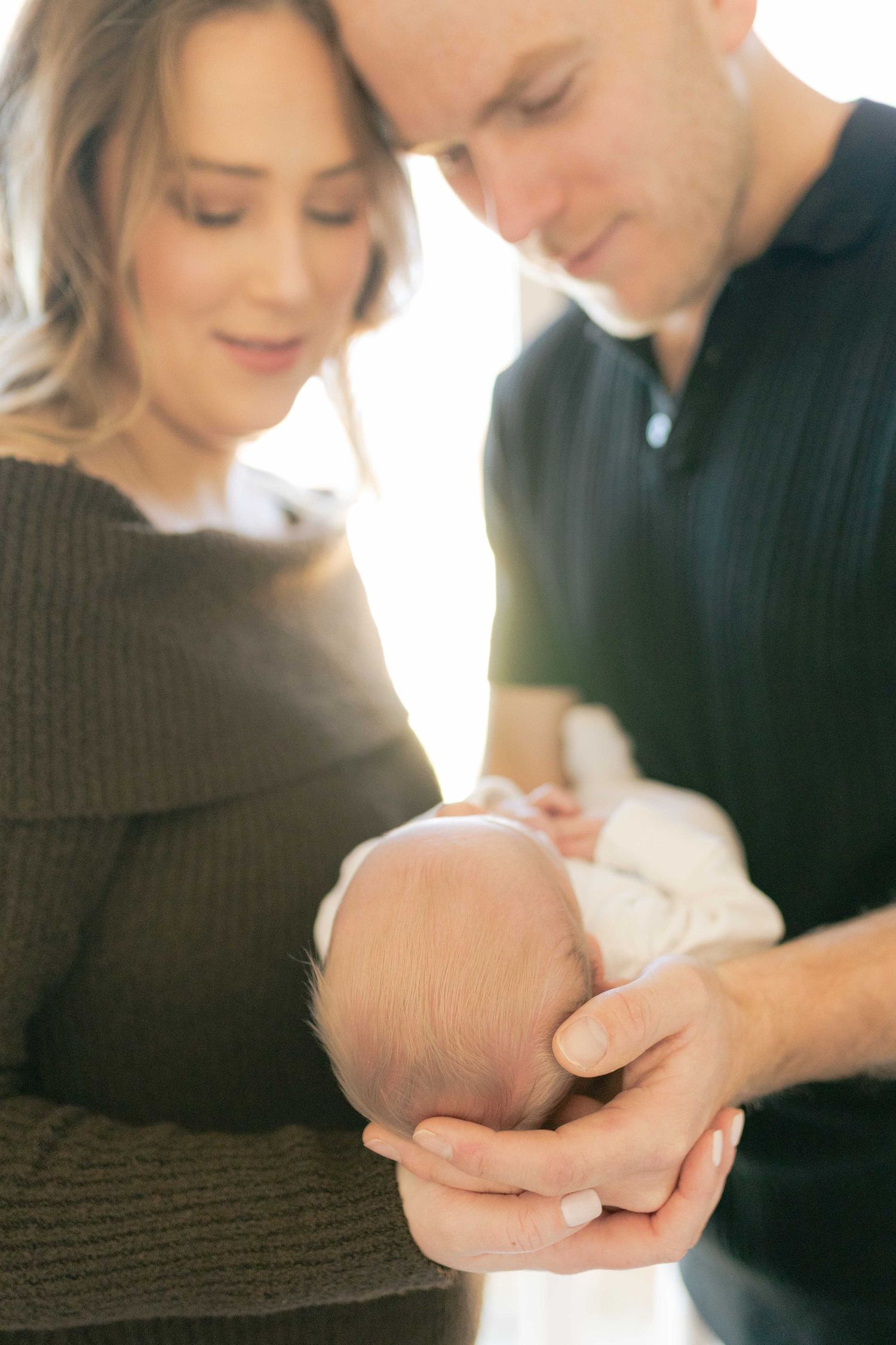Parents smiling at each other holding their newborn between their hands