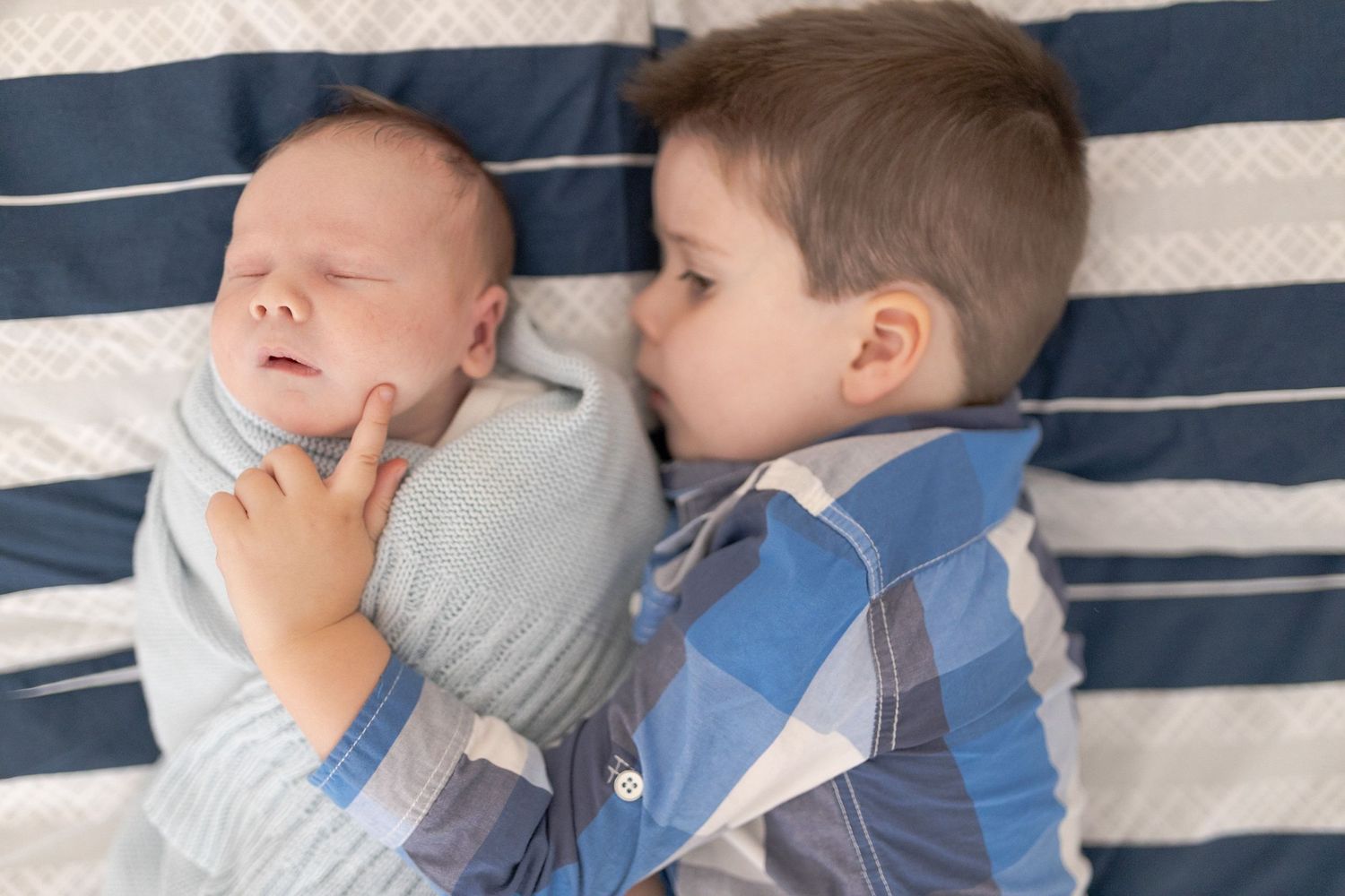 Brothers lying on the bed snuggled together while lying on the bed baby swaddled in blue blanket at home newborn session  Moonee Ponds Melb