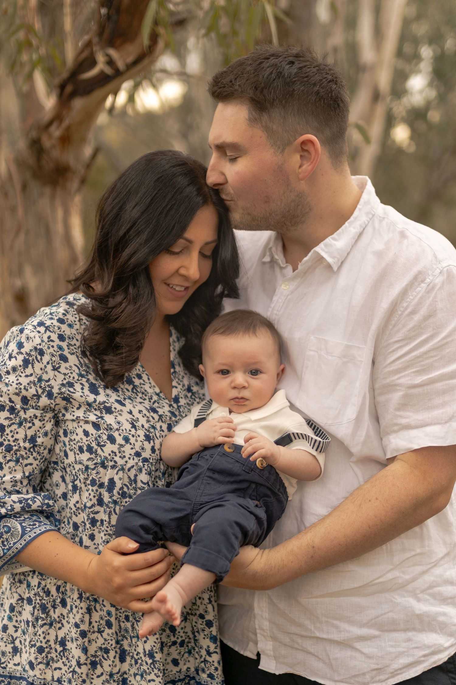 First time parents holding newborn in the bushland with tall grass. Dad kissing on mums head Outdoor family session Sunshine North Melb Vic
