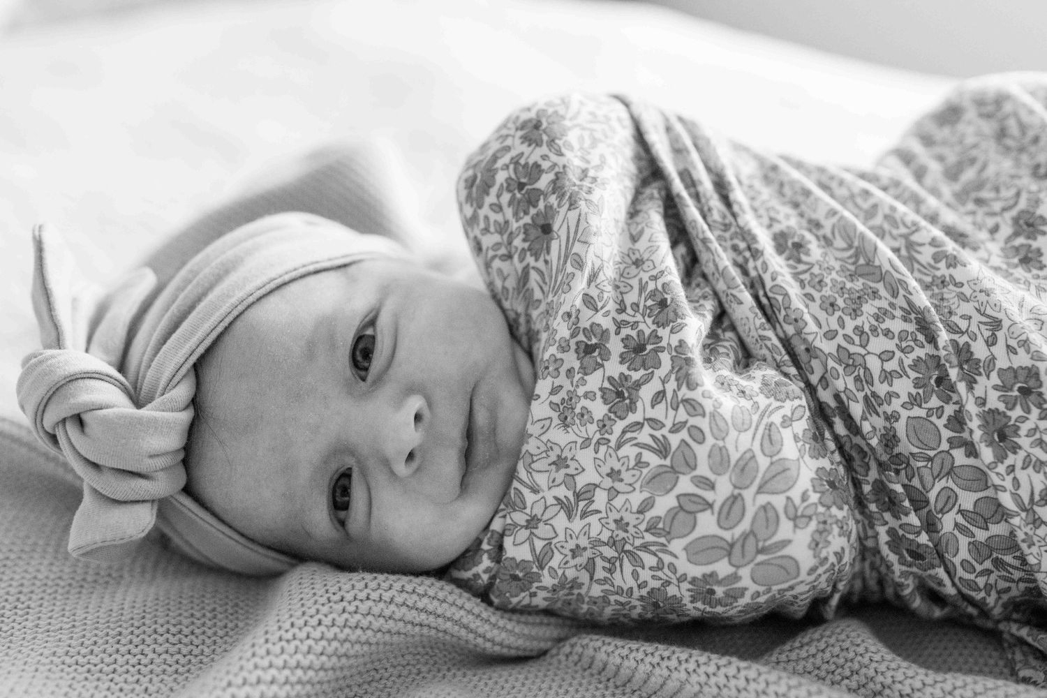 Newborn baby girl wrapped up in floral swaddle lying on the bed. At home newborn session Tullamarine Melb Vic