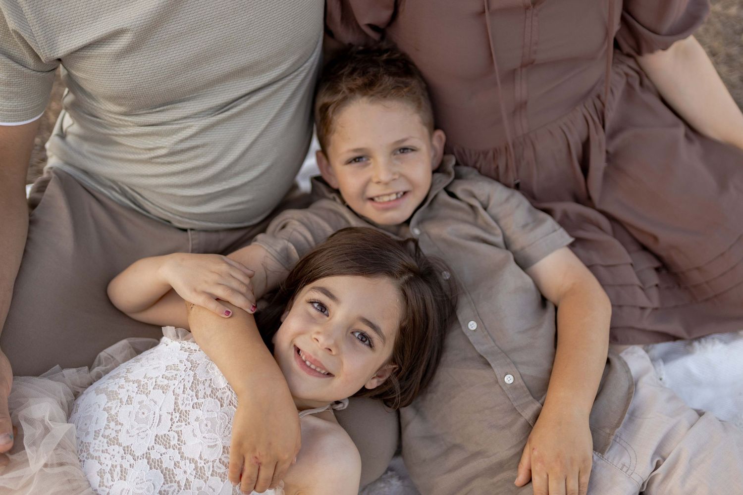 Family of four sitting on a white blanket on a hill with fields in the background Outdoor at home family session Gisborne Melb Vic