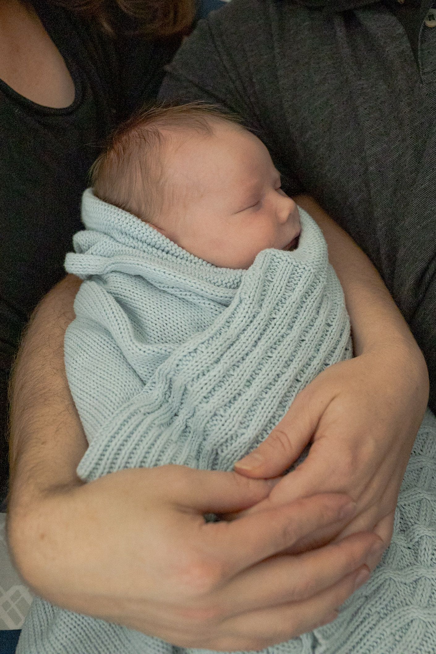 Parents snuggling newborn baby boy while lying on the bed baby swaddled in blue blanket at h ome newborn session  Moonee Ponds Melb Vic