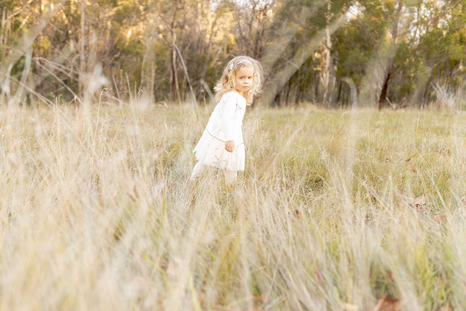 Little girl walking through a field of tall grass with windswept hair. Outdoor family session Macedon Ranges Melb Vic