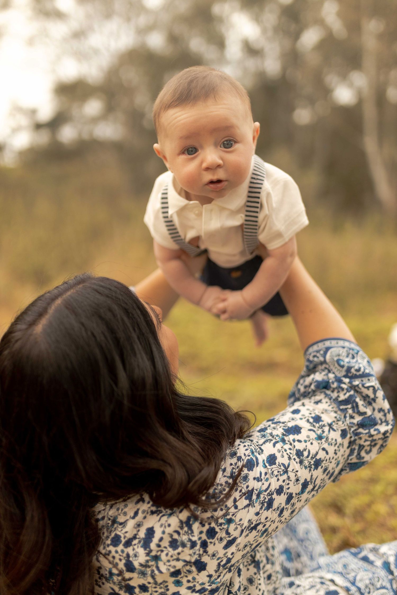 Newborn baby boy being held up in the air by his mum warm sunlight looking surprised. Outdoor family session Sunshine North Melb Vic