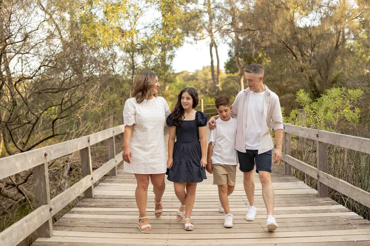 Family walking across a bridge happy all holding onto each other. Family of four parents and two older children, Newport,Melbourne, Victoria