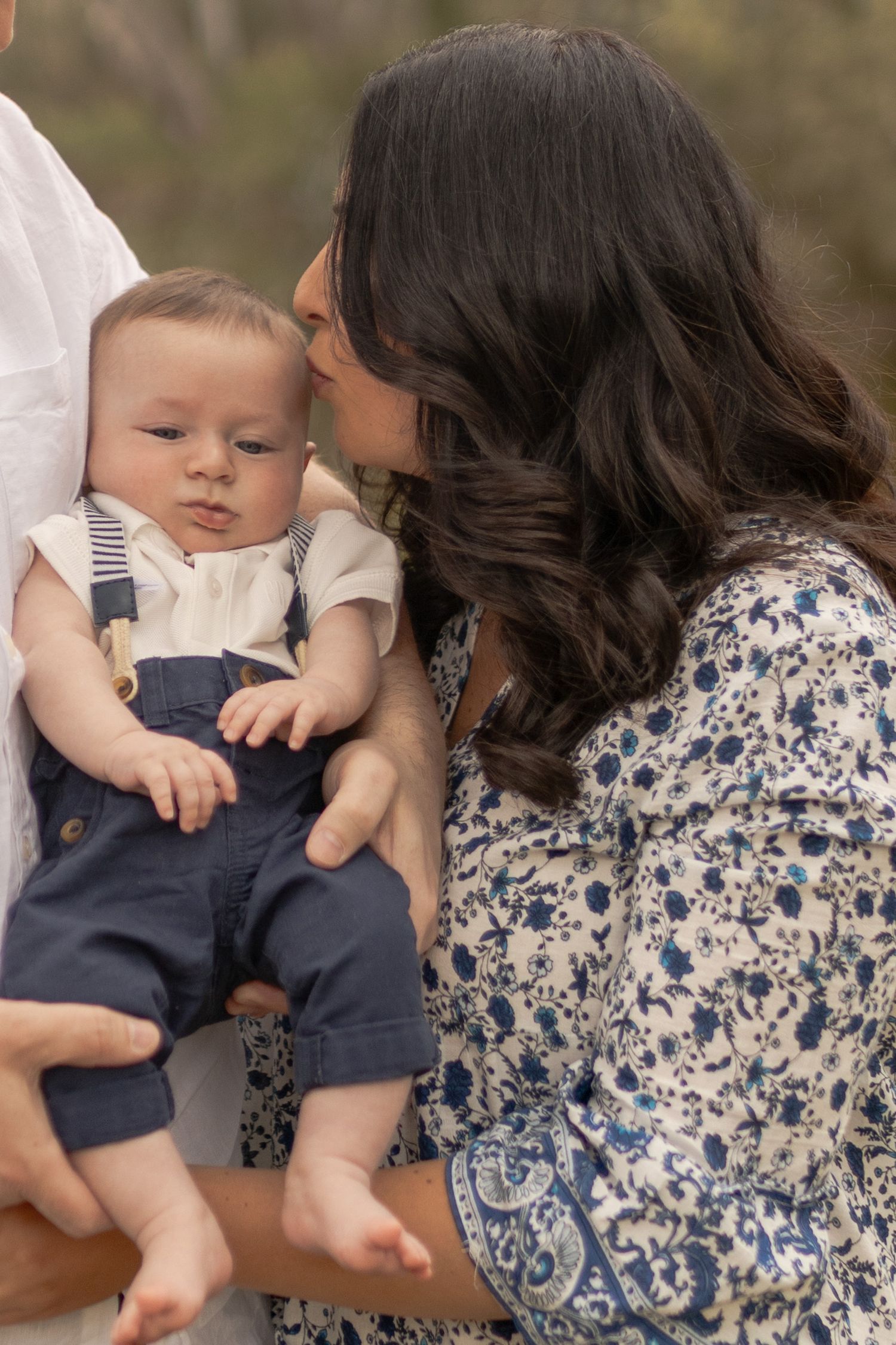 Mum kissing baby boy on the head while dad is holding him Outdoor family session Sunshine North Melb Vic