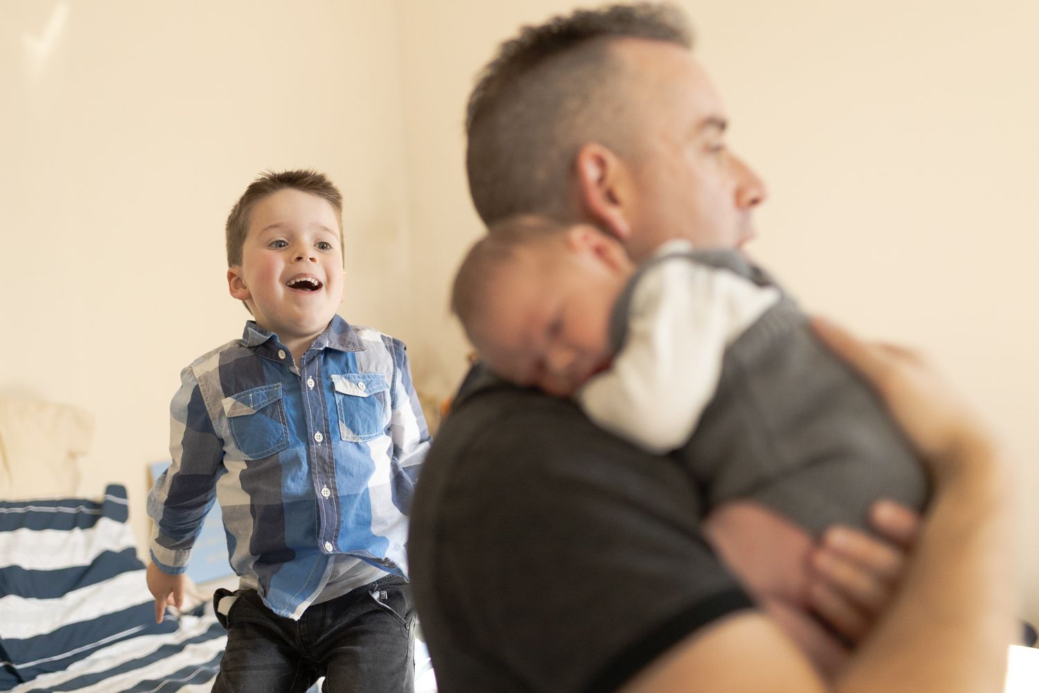 Dad holding baby boy big brother jumping on the bed smiling  at home newborn session  Moonee Ponds Melb