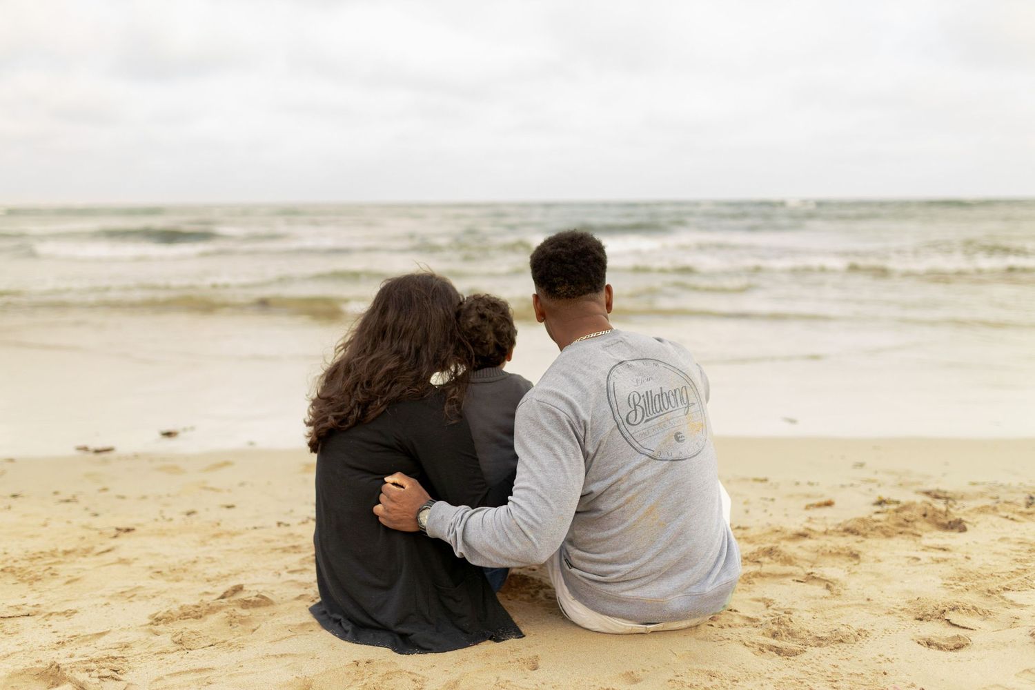 Family of three sitting on the sand looking at the water Outdoor family session Torquay