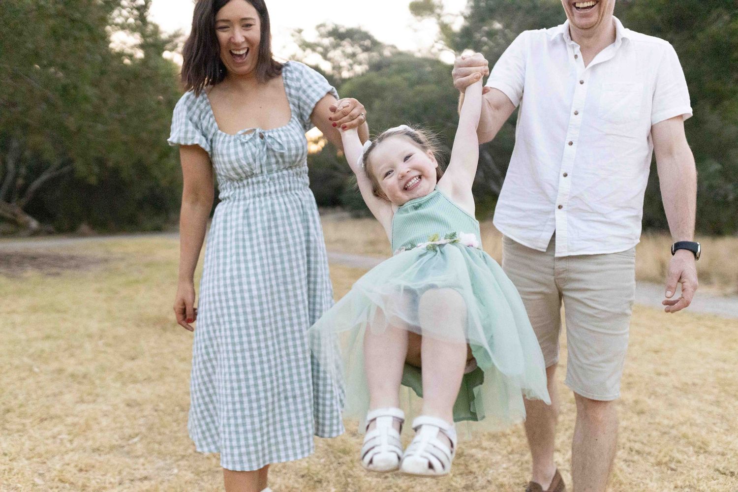 Mum and dad swinging their daughter happily smiling and laughing, Newport Lakes, Melb, Vic