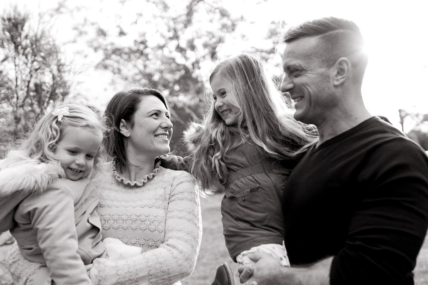 Family of four holding each other happily looking at each other 2 girls outdoor family session Macedon Ranges, Melbourne, Victoria