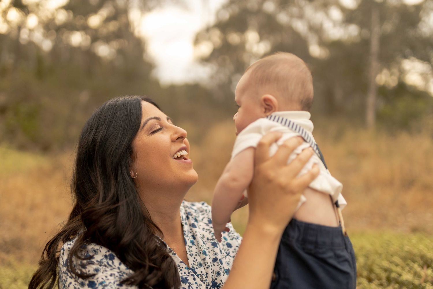 Newborn baby boy being held up in the air by his mum warm sunlight mum has a big smile Outdoor family session Sunshine North Melb Vic