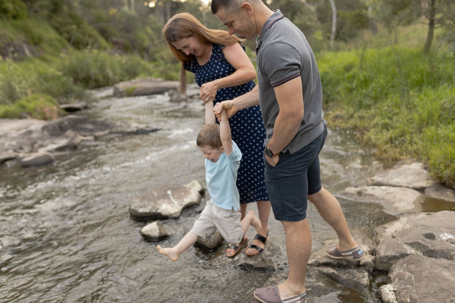 Parents holding toddlers hands over walking over the creek being playful. outdoor maternity session. Coburg Lake Melb Vic
