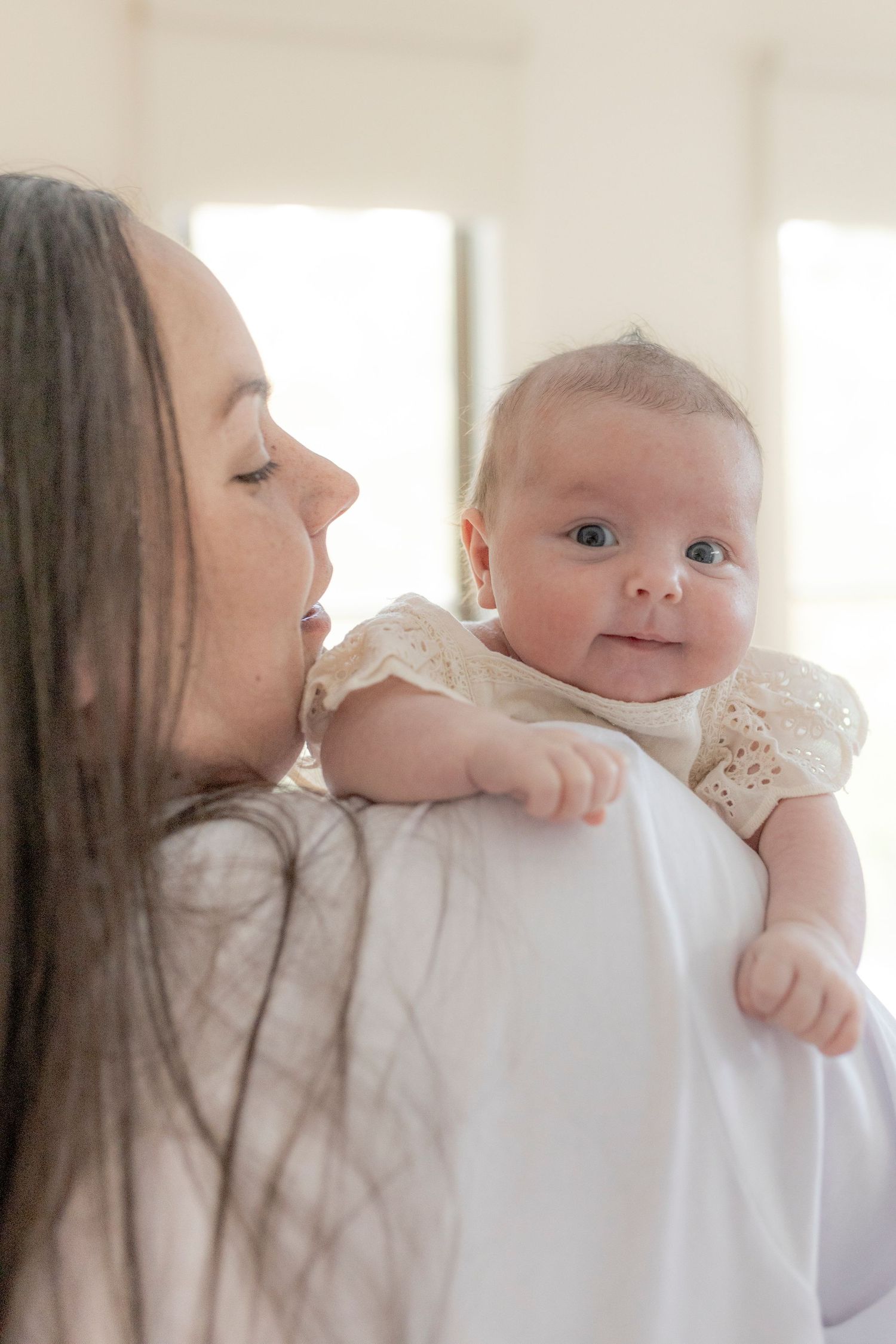 Newborn baby girl smiling over her mums shoulder