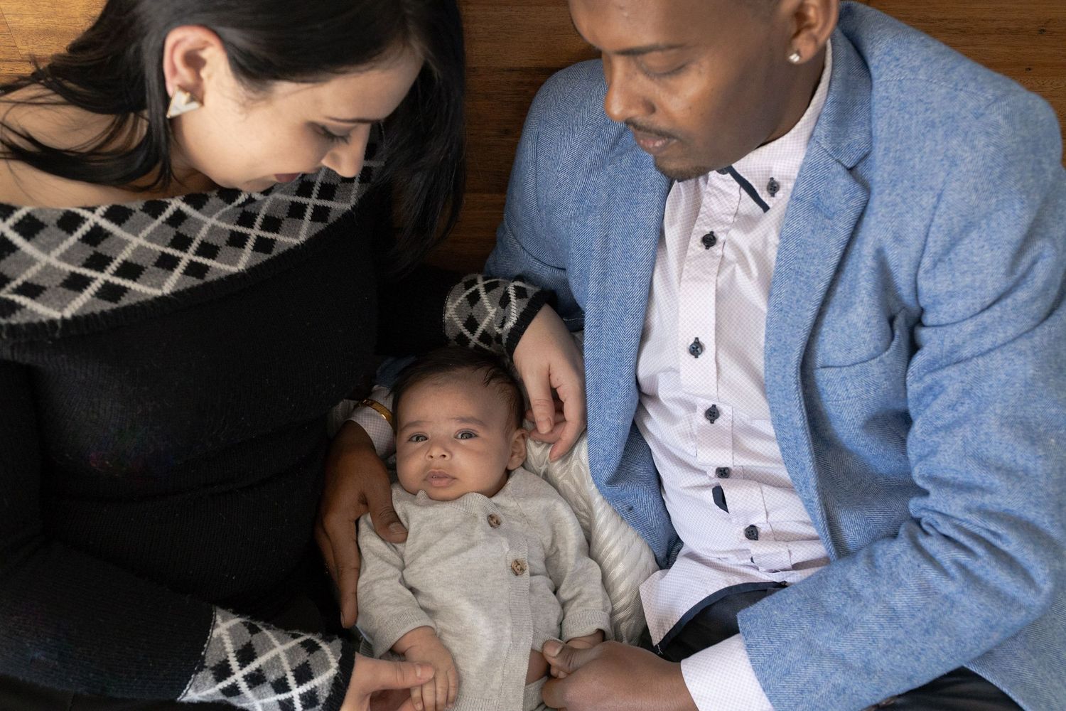 Parents looking down at baby boy lying on the bed snuggles together. At home family session, sunshine north melb vic