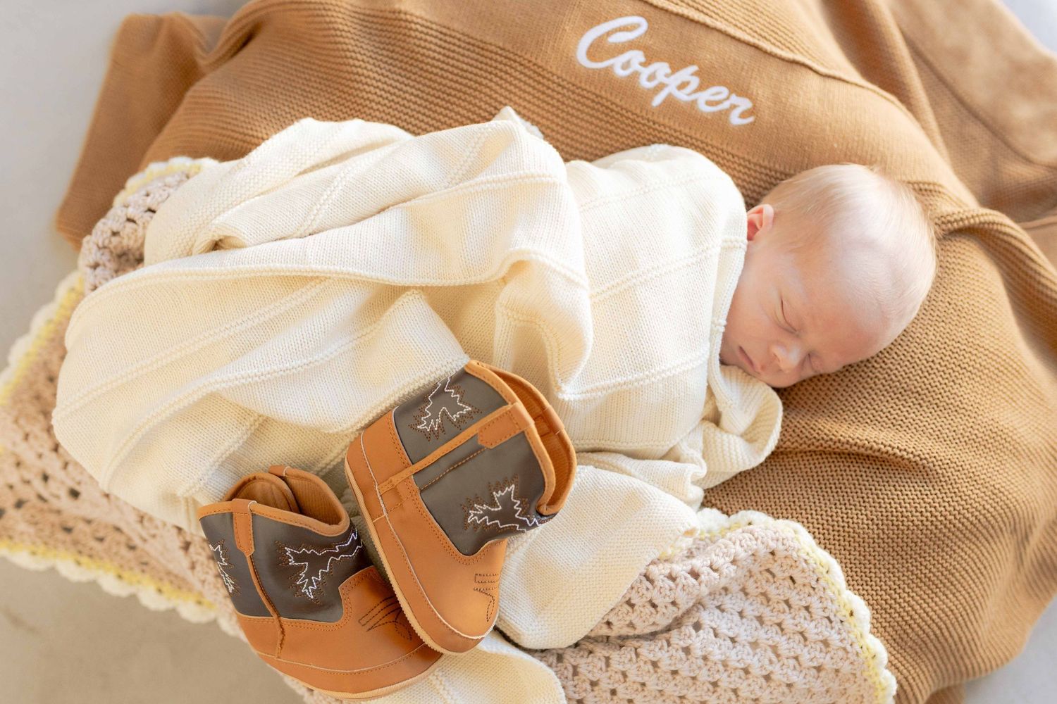 Newborn close up lying on top off the warm blankets with a pair of small cowboy boots
