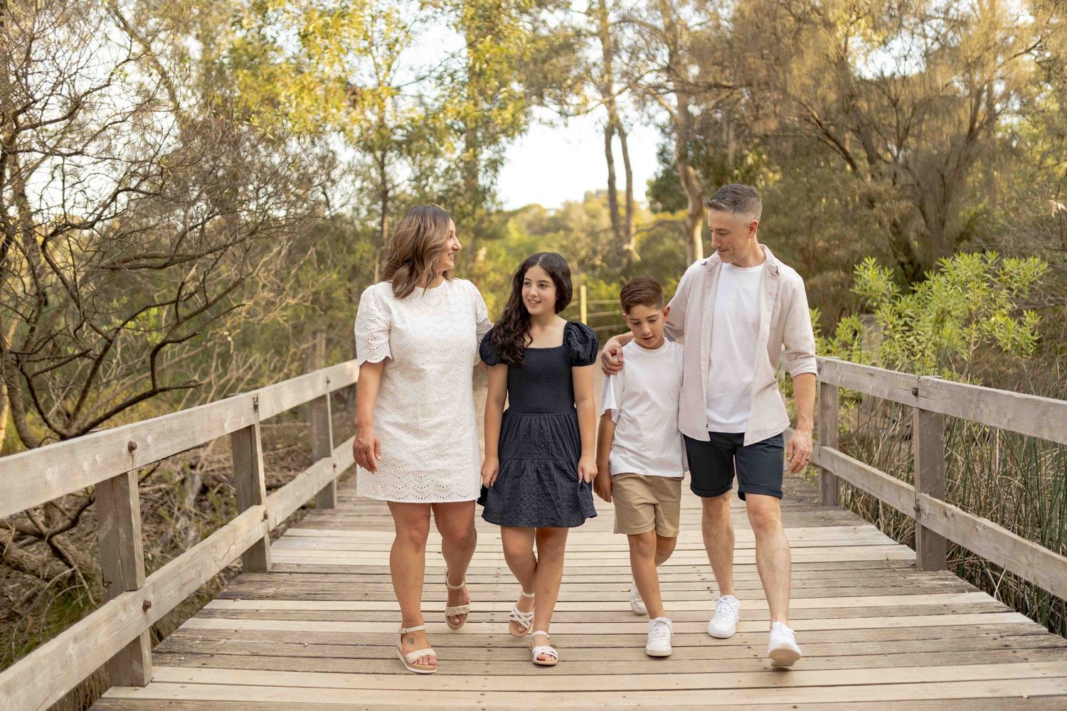 Family walking across a bridge happy all holding onto each other. Family of four parents and two older children, Newport,Melbourne, Victoria