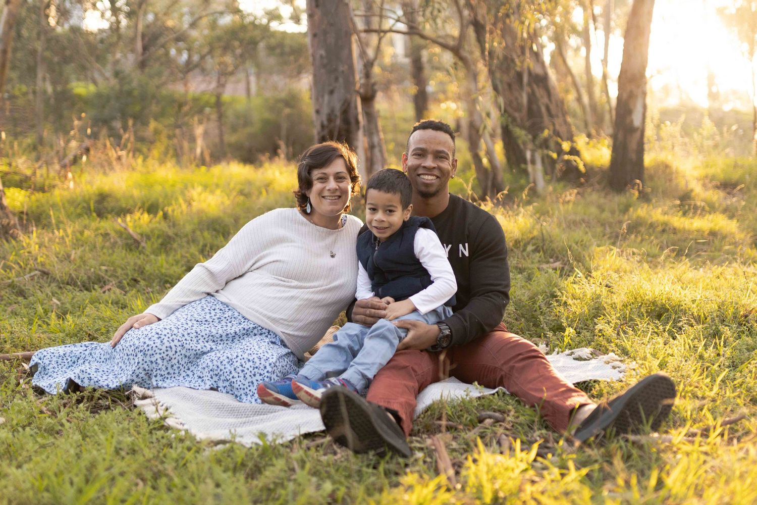Family of three on a white blanket smiling Outdoor maternity session Sunshine Melb Victoria