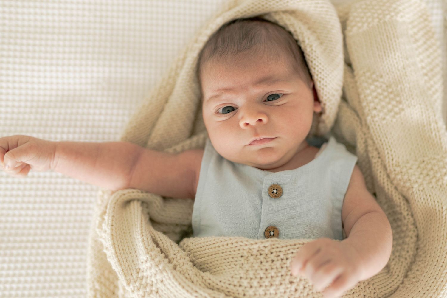 Newborn surrounded by a soft blanket and stretching arm out
