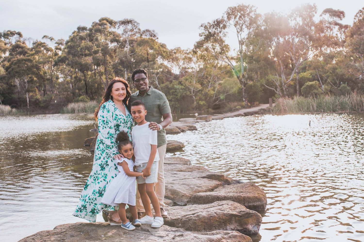 Family of four holding each other happily standing on the large rocks, looking at each other. Newport Lakes, Melbourne, Victoria