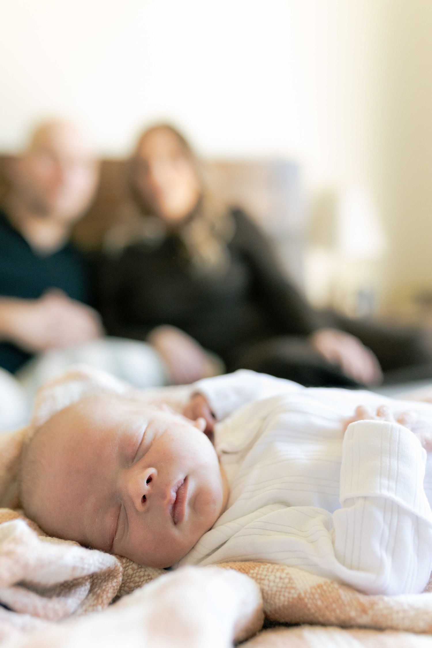 Newborn in focus parents blurred in the background sitting on the bed Melbourne's West Newborn Photography