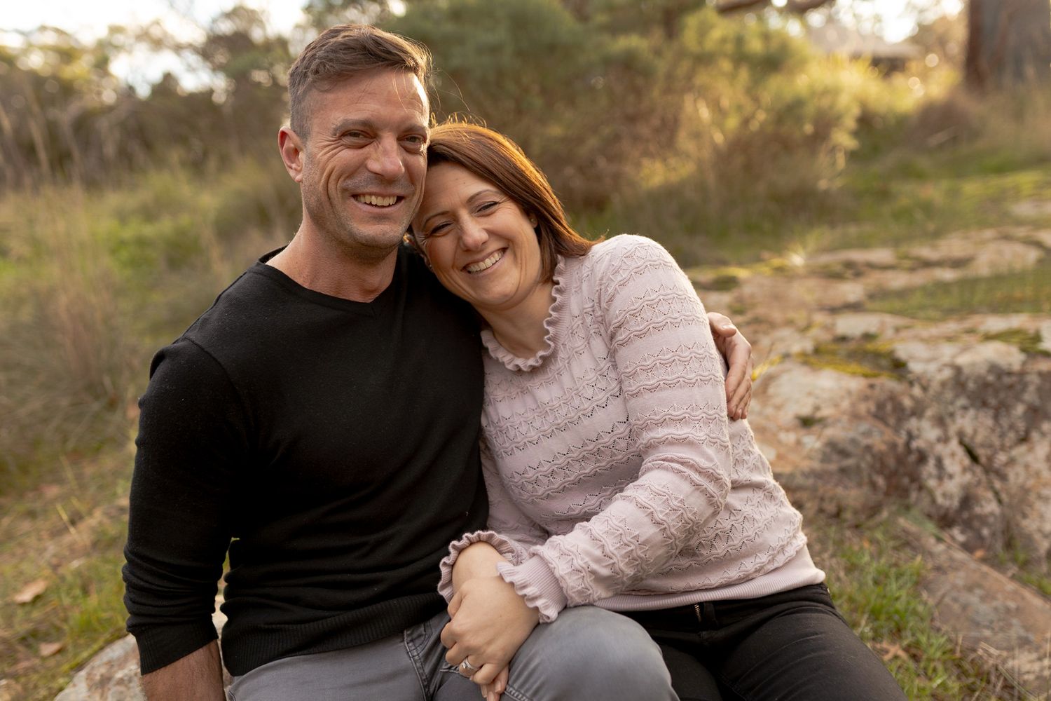 Couple sitting together smiling looking at chidlren Girl twirling in a field big smile Outdoor family session Macedon Ranges Melb Vic