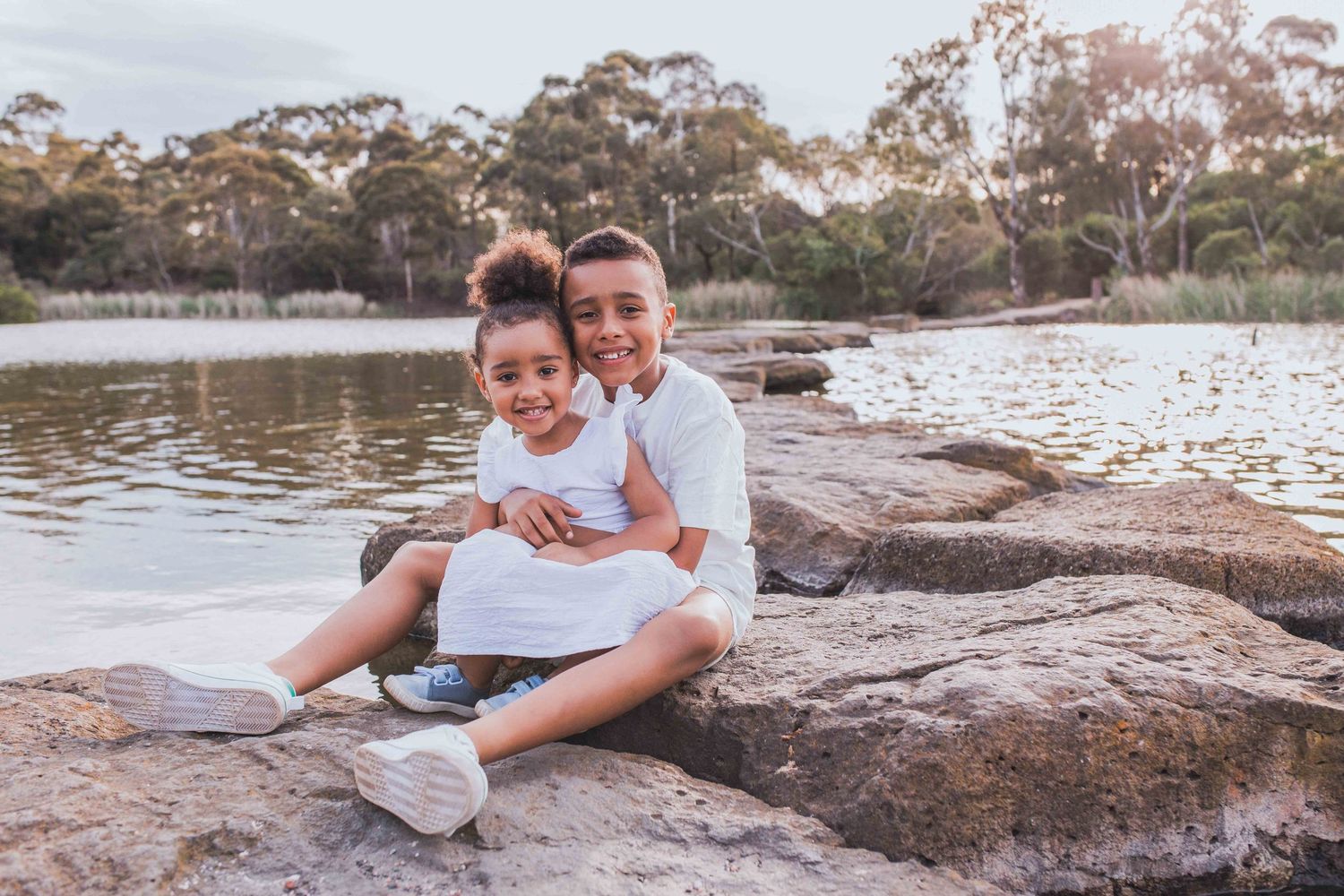Brother and sister hugging sitting on the rocks across a lake Newport Lakes, Melbourne, Victoria
