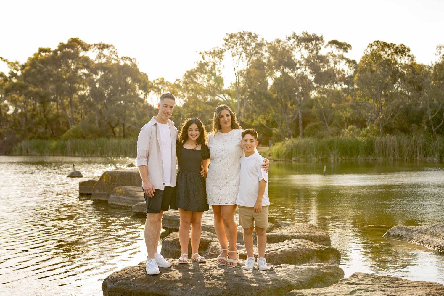 Family of four holding each other happily standing on the large rocks, looking at each other. Newport Lakes, Melbourne, Victoria