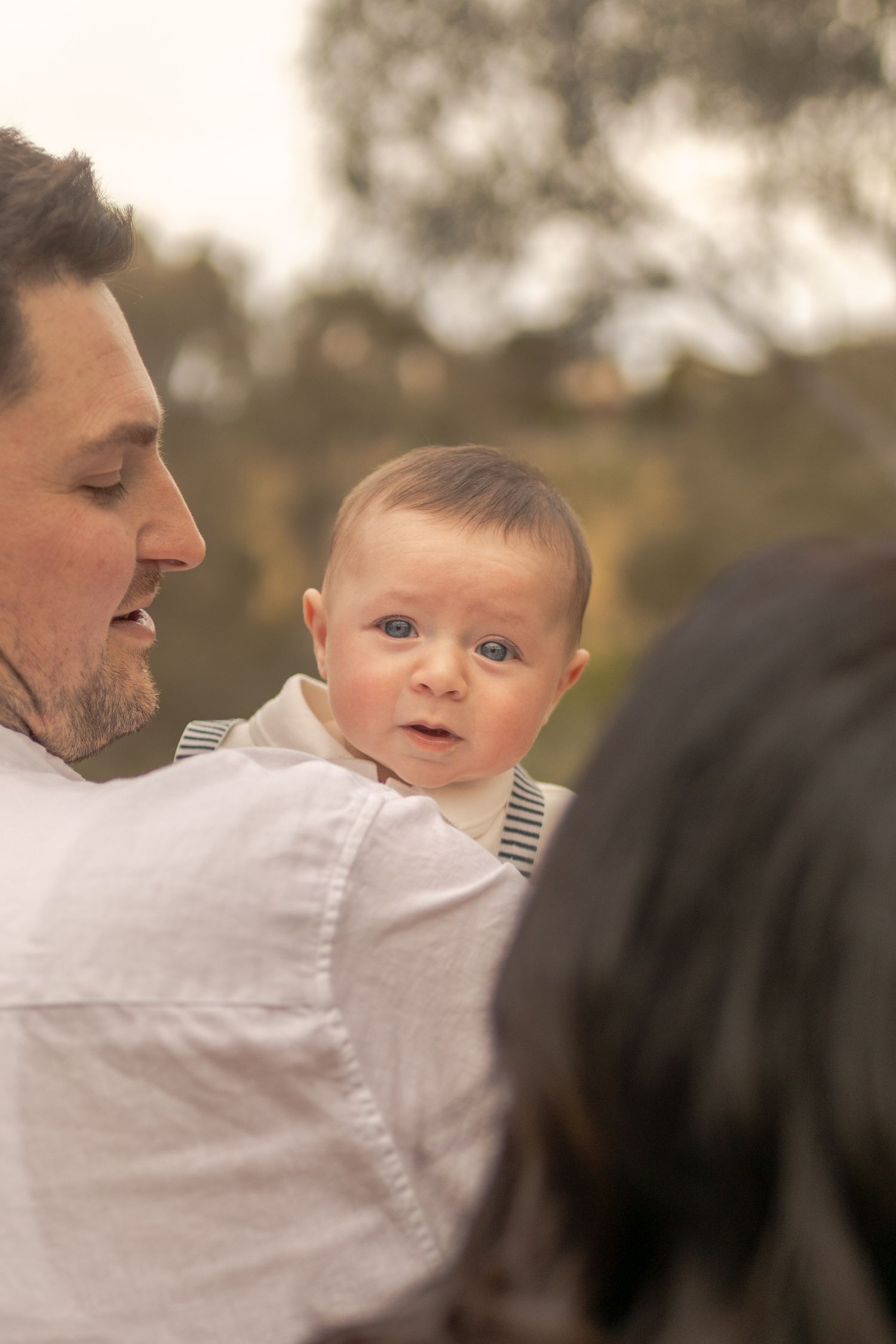 Baby boy peering over dad's shoulder crying outdoor family session Sunshine North Melb Vic