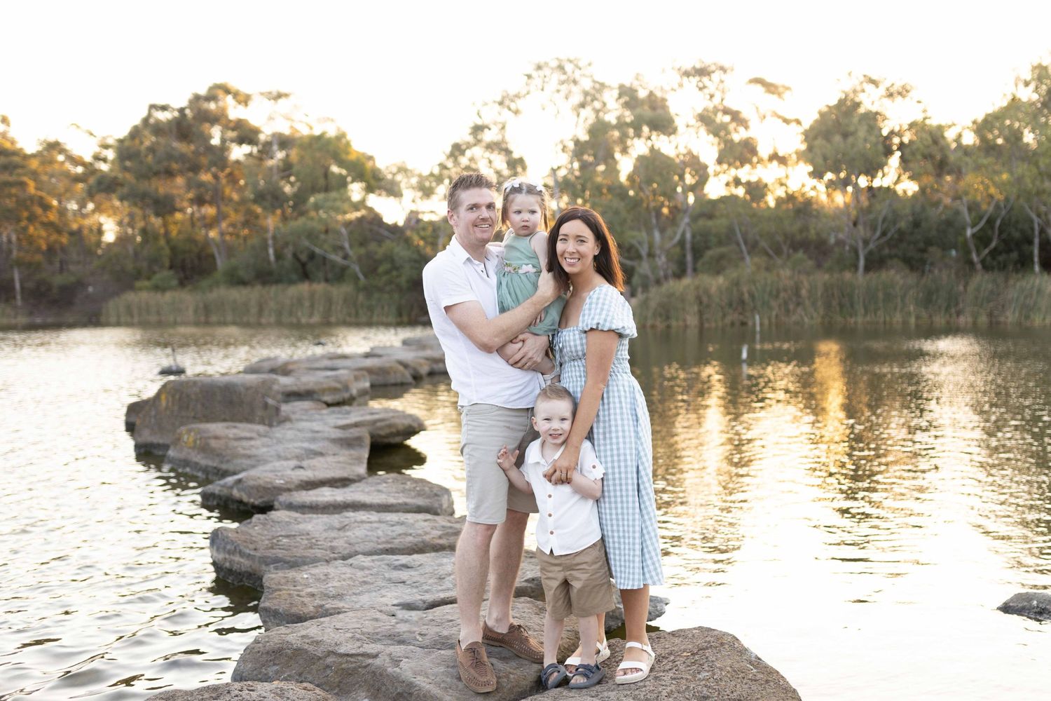 Family of four holding each other happily standing on the large rocks, looking at each other. Newport Lakes, Melbourne, Victoria