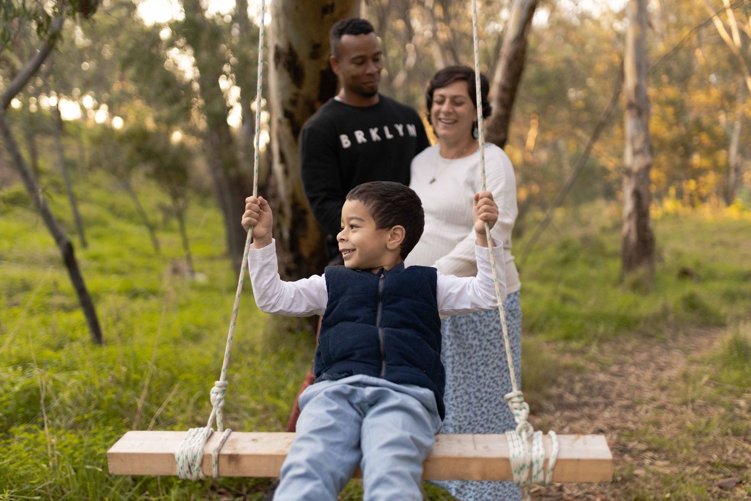 Son on the swing with parents behind Outdoor maternity session Sunshine Melb Victoria