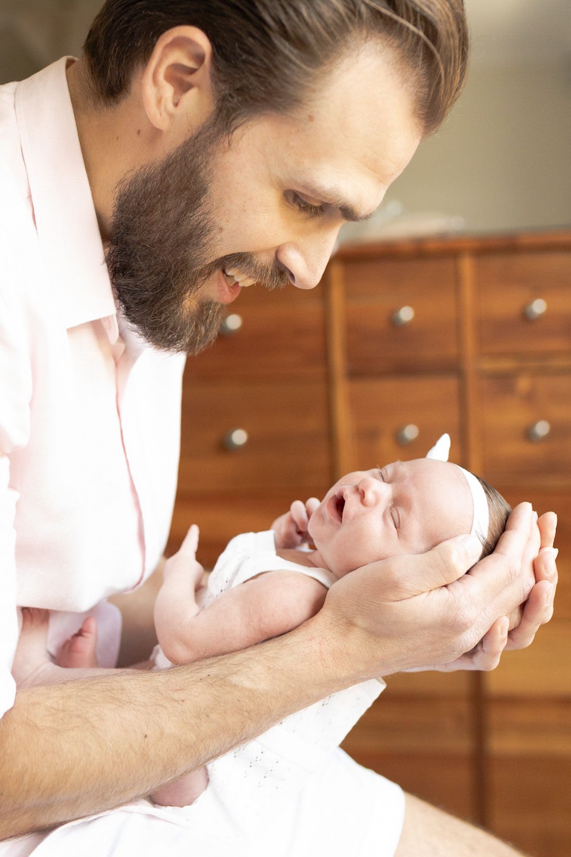 Dad holding newborn baby girl in his hands while dad is looking down at home newborn session Caroline Springs Melb Victoria