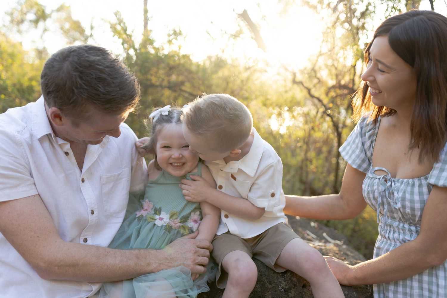 Siblings cuddling brother kissing his sister parents looking on, Outdoor family session  Newport Lakes, Melb, Vic