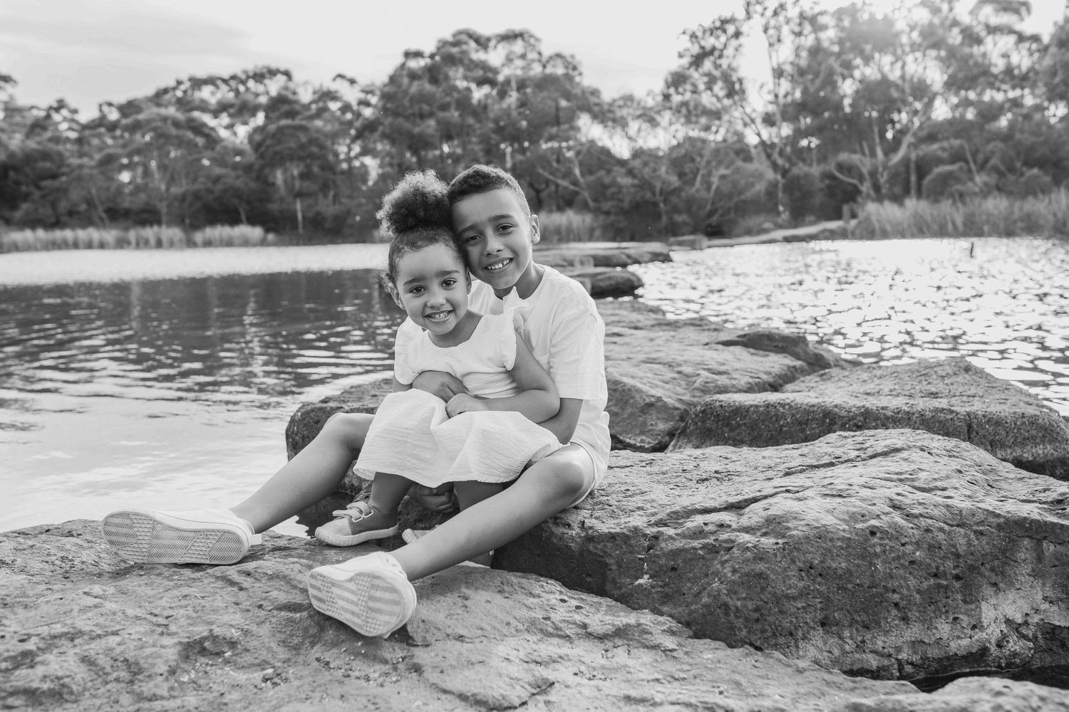 Brother and sister hugging sitting on the rocks across a lake outdoor family session  Newport Lakes, Melbourne, Victoria