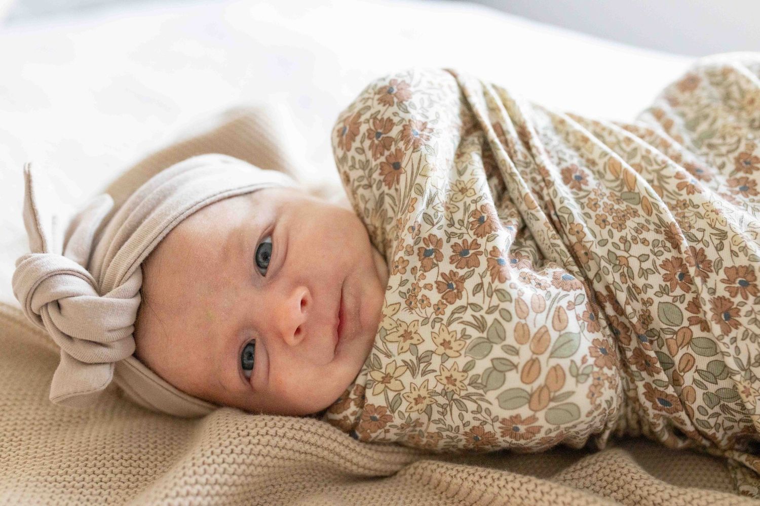 Newborn baby girl wrapped up in floral swaddle lying on the bed. At home newborn session Tullamarine Melb Vic