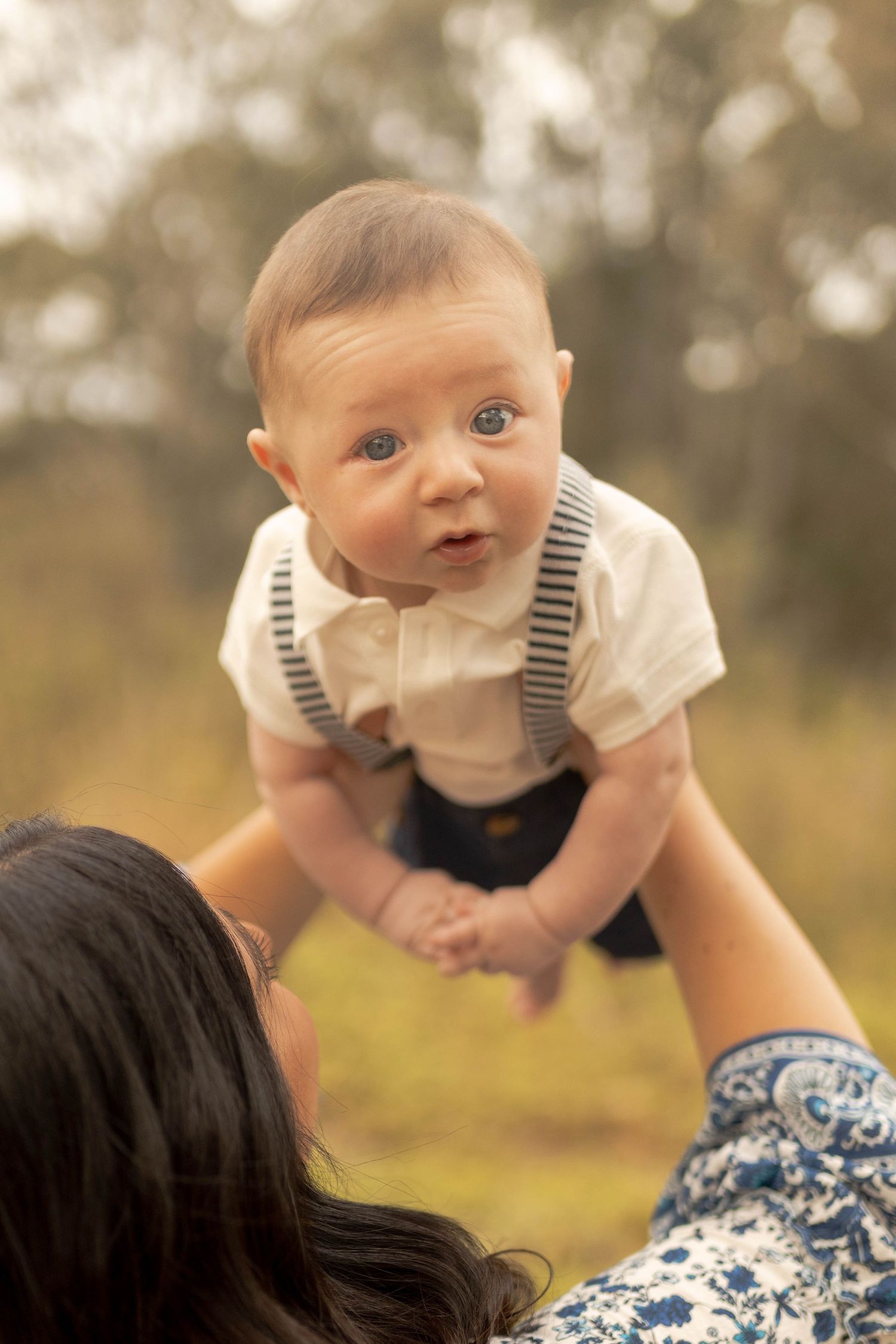 Newborn baby boy being held up in the air by his mum warm sunlight looking surprised. Outdoor family session Sunshine North Melb Vic