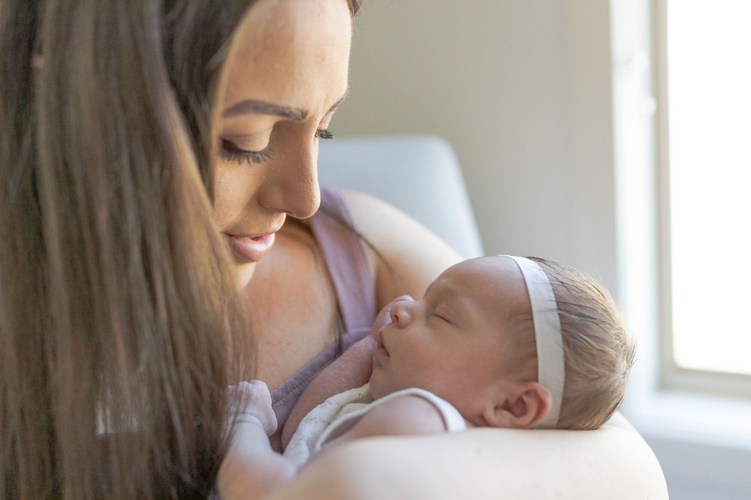 Mum holding her newborn baby girl in her arms looking at her sitting in a rocking chair at home newborn session Caroline Springs Melb Vic