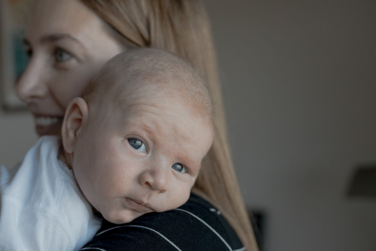 Newborn baby boy looking over his mother's shoulder cheek squished At home newborn session Gisborne Melb Vic