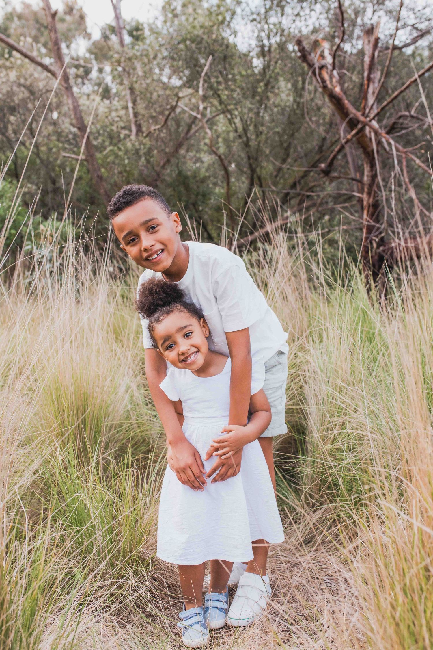 Siblings hugging in tall grass gamily outdoor session, Newport Lakes Melb Vic