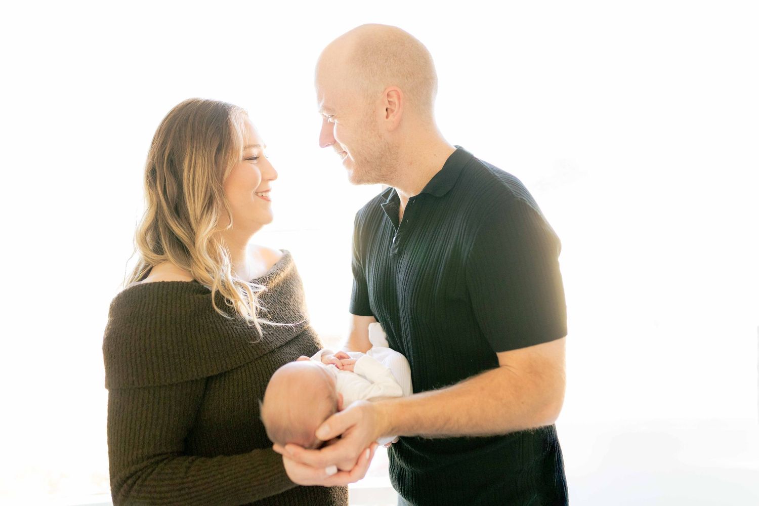 Parents smiling at each other holding their newborn between their hands